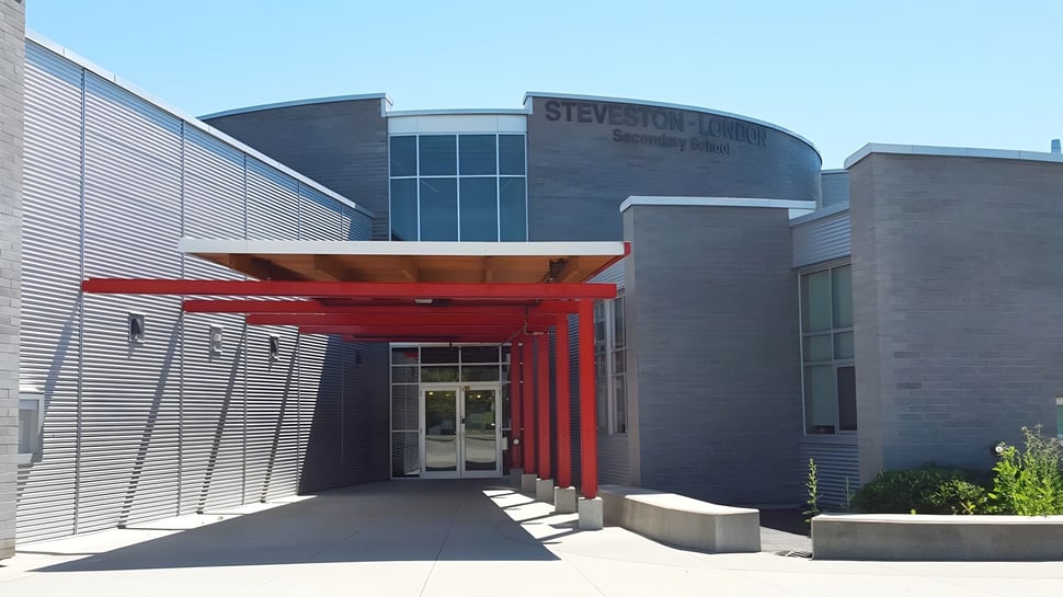 Das mehrstöckige Gebäude der Steveston-London Secondary School zeigt einen roten Eingang mit großen Fenstern und einer gepflasterten Außenanlage.