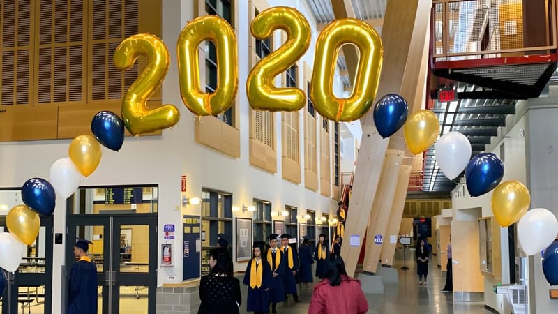 Schülerinnen und Schüler der Steveston-London Secondary School stehen in einer Halle unter großen goldenen 2020-Luftballons in ihren Abschlussroben.