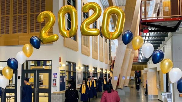 Schülerinnen und Schüler der Steveston-London Secondary School stehen in einer Halle unter großen goldenen 2020-Luftballons in ihren Abschlussroben.