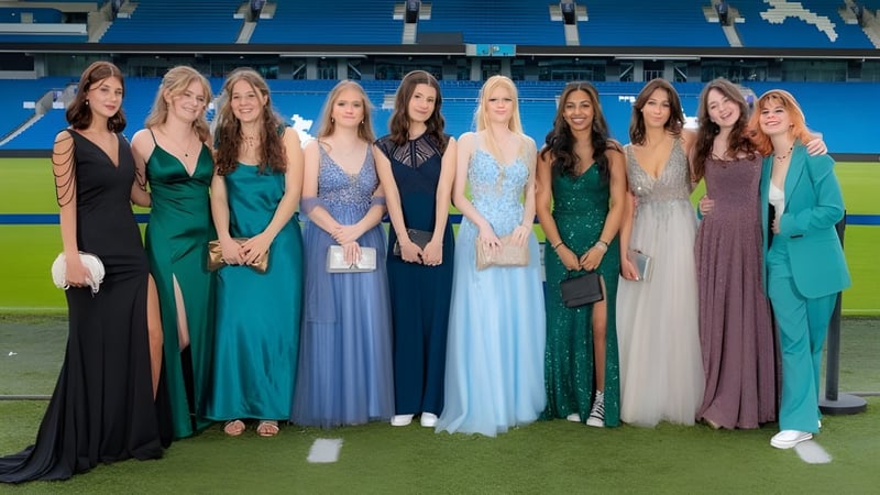 Eine Gruppe junger Schülerinnen in Festkleidern steht auf dem Sportplatz der Steyning Grammar School and Sixth Form mit dem Stadion im Hintergrund.