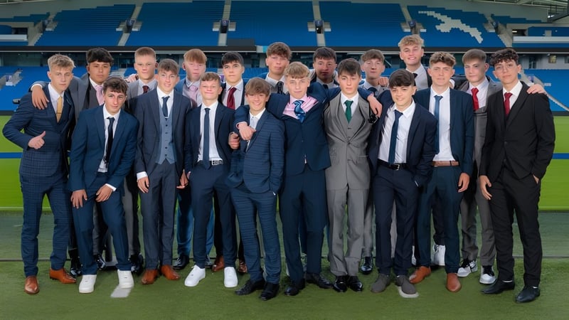 Eine Gruppe junger Männer in formeller Kleidung steht auf dem Sportfeld der Steyning Grammar School and Sixth Form mit einem großen Stadion im Hintergrund.