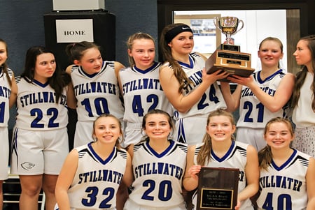 Eine Gruppe junger Basketballspielerinnen der Stillwater Christian School feiert mit einem Pokal ihren Sieg in der Umkleidekabine.