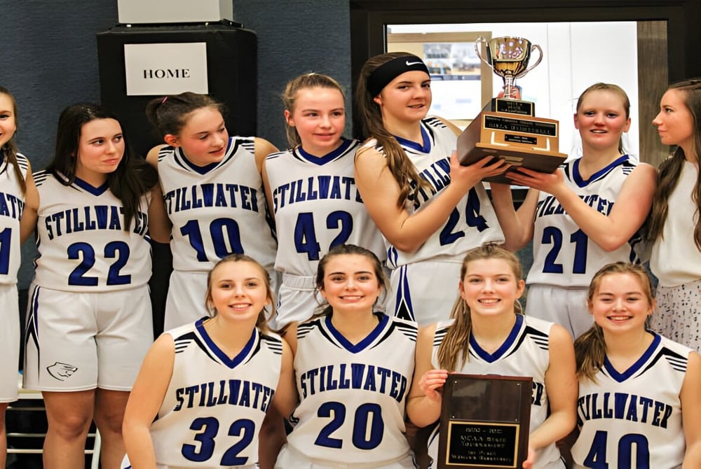 Eine Gruppe junger Basketballspielerinnen der Stillwater Christian School feiert mit einem Pokal ihren Sieg in der Umkleidekabine.