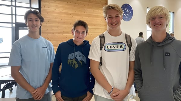 Vier Schülerinnen und Schüler stehen gemeinsam vor einer Wand mit Logo auf dem Campus der Stillwater Christian School.