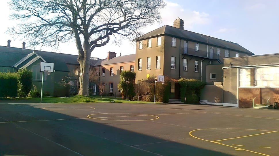 Das mehrstöckige Backsteingebäude der St. Mary’s Secondary School in Baldoyle mit einem Basketballplatz im Vordergrund und umgeben von Bäumen.
