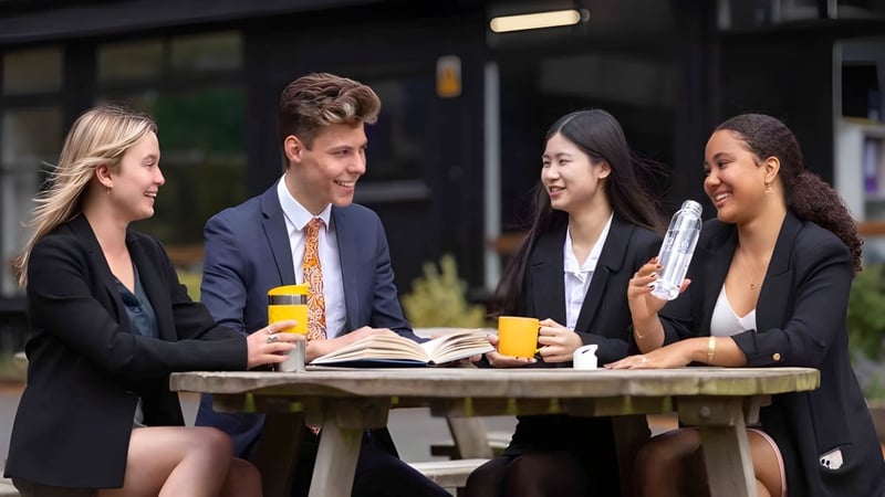 Vier junge Erwachsene führen eine Gesprächsrunde am Außentisch auf dem Campus des Stoke College.