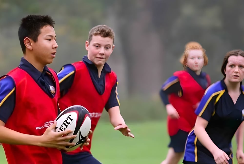 Eine Gruppe Schüler in Sportuniformen spielt Rugby auf dem Sportfeld des Stoke College.