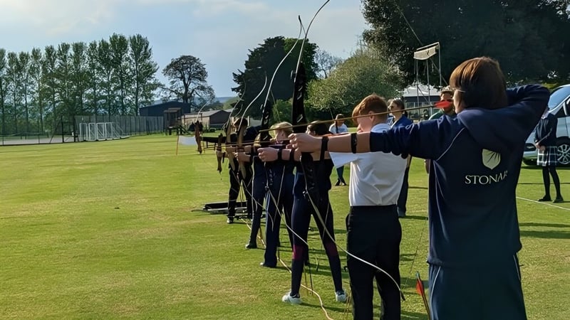 Schüler der Stonar School stehen auf einem Feld und schießen mit Bögen auf Zielscheiben.
