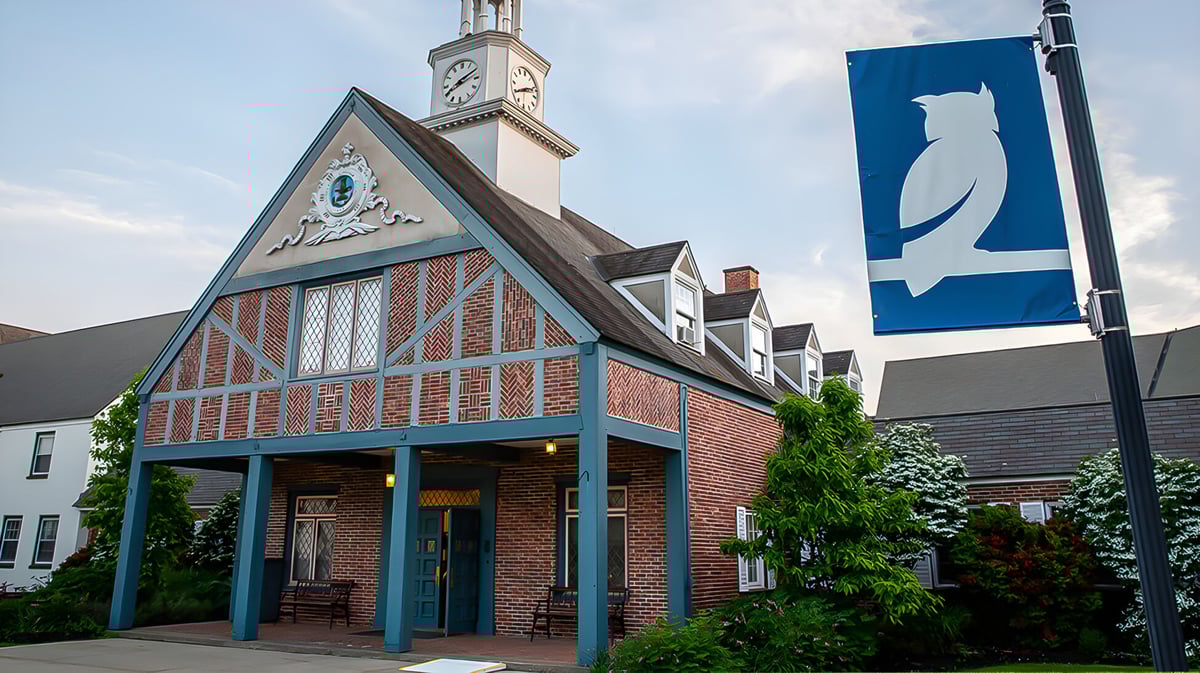 Ein historisches Backsteingebäude mit einem Uhrenturm steht auf dem Gelände der Stoneleigh-Burnham School umgeben von grünen Bäumen.