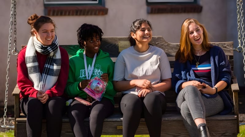 Vier Schuelerinnen sitzen auf einer Holzbank und unterhalten sich auf dem Campus der Stoneleigh-Burnham School.