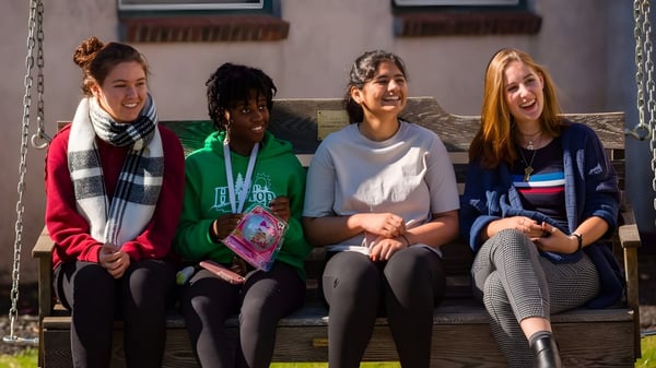 Vier Schuelerinnen sitzen auf einer Holzbank und unterhalten sich auf dem Campus der Stoneleigh-Burnham School.