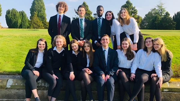 Eine Gruppe Schülerinnen und Schüler des Stonyhurst College versammelt sich im grünen Außenbereich mit Bäumen und Gras.