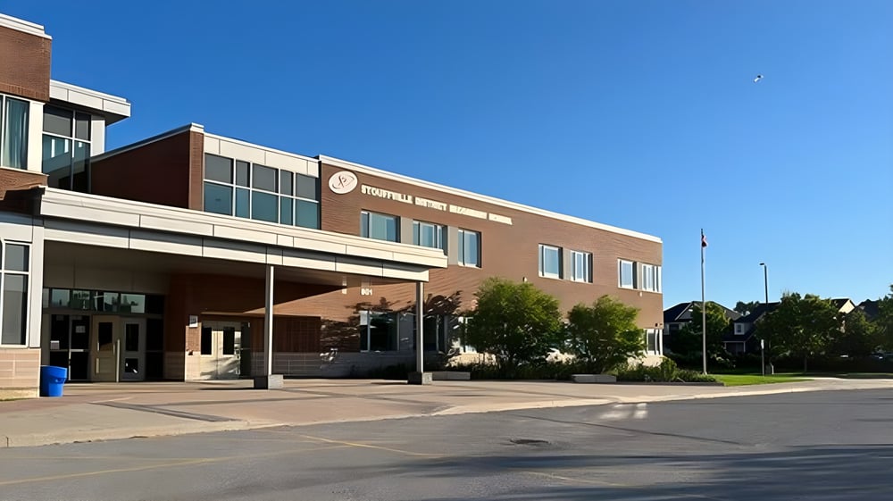 Das große Backsteingebäude mit dem Haupteingang der Stouffville District Secondary School ist von Bäumen und einem gepflasterten Bereich umgeben.