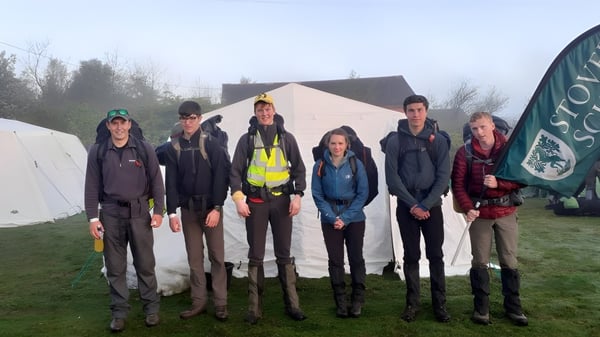 Eine Gruppe von Personen steht vor Zelten auf einer Wiese auf dem Gelände der Stover School.