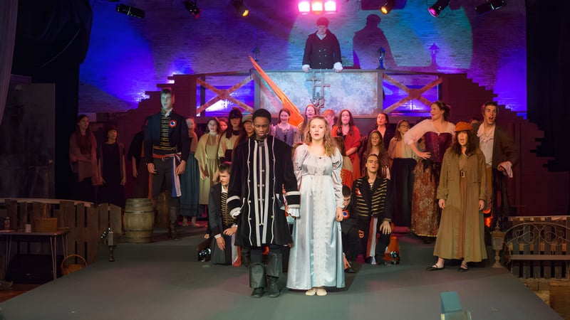 Schüler der Stover School stehen in auffälligen Kostümen auf einer Bühne mit bunter Beleuchtung und dekorativem Hintergrund.