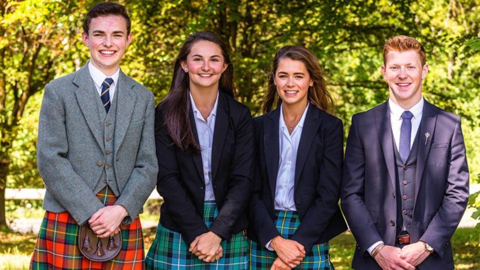 Vier Personen in formeller Kleidung stehen gemeinsam in einem grünen Außenbereich auf dem Campus des Stratford College.