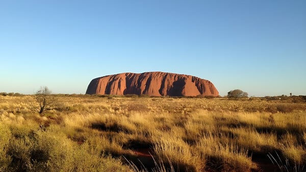 Eine markante rote Sandsteinformation erhebt sich vor blauem Himmel über einer Graslandschaft nahe dem Stretton State College.