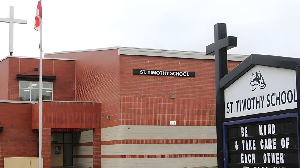 Das ziegelrote Hauptgebäude der St. Timothy High School zeigt deutlich den Schulnamen neben einer Fahne und einem großen kreuzförmigen Bauwerk.