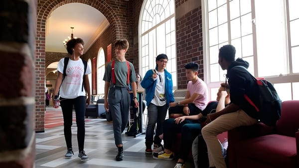 Eine Gruppe von Schülerinnen und Schülern steht und sitzt im Flur der Stuart Hall School mit Ziegelwänden und großen Fenstern.