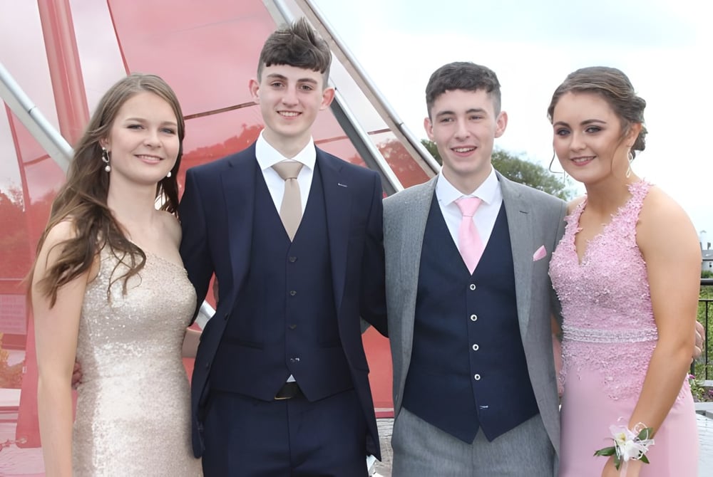 Vier Personen in formeller Kleidung stehen gemeinsam vor einem roten Gebäude auf dem Campus des Summerhill College.