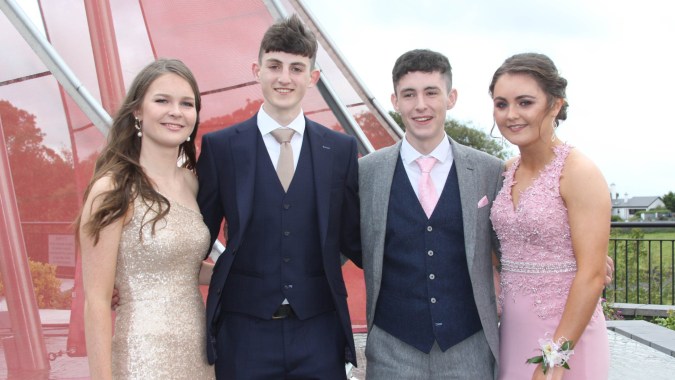 Vier gut gekleidete Personen posieren vor einem roten Gebäude auf dem Campus des Summerhill College.