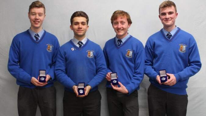 Vier Schüler in blauen Uniformen stehen mit kleinen Boxen auf dem Gelände des Summerhill College.