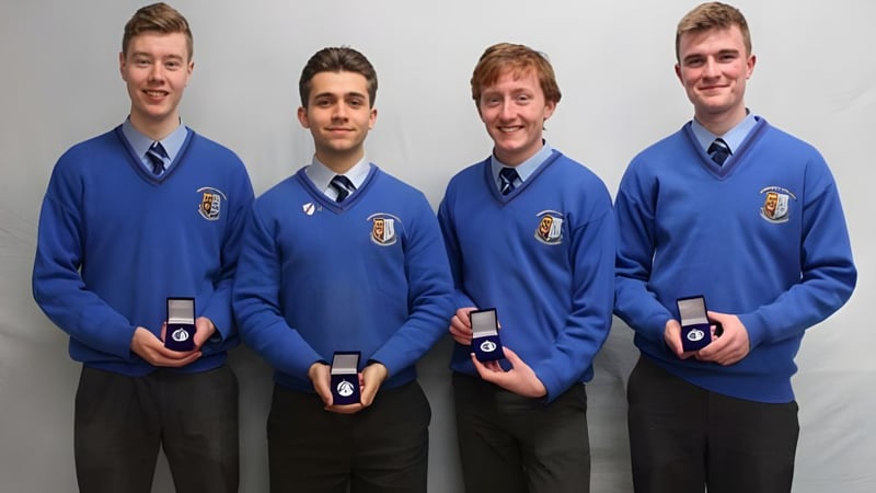 Vier Schüler des Summerhill College tragen blaue Uniformen und halten kleine Boxen mit Ringen vor neutralem Hintergrund.