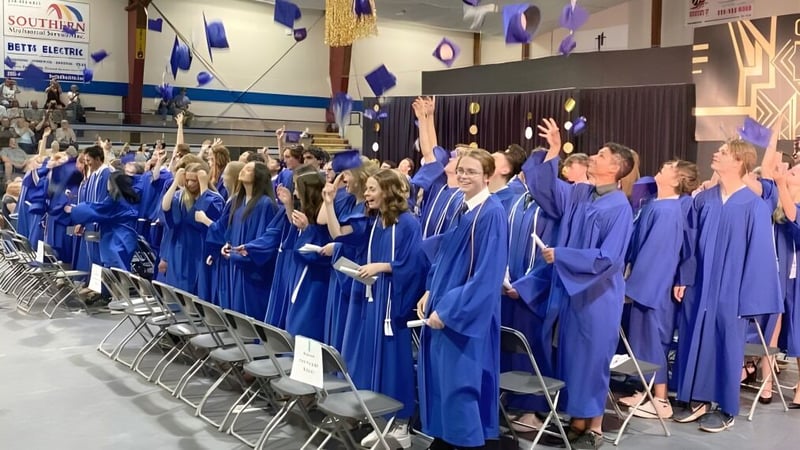 Eine große Gruppe von Absolventinnen und Absolventen der Summerland Secondary School trägt blaue Talare und Mützen bei der Abschlussfeier.