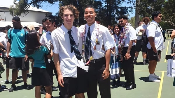 Eine Gruppe Schüler steht zusammen draußen auf dem Campus der Sunnybank State High School mit Bäumen und Gebäuden im Hintergrund.