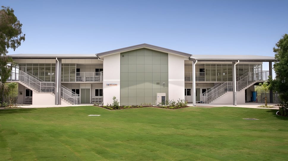 Das moderne zweistöckige Gebäude der Sunshine Beach State High School steht auf einem gepflegten Rasen und ist von grüner Vegetation umgeben.