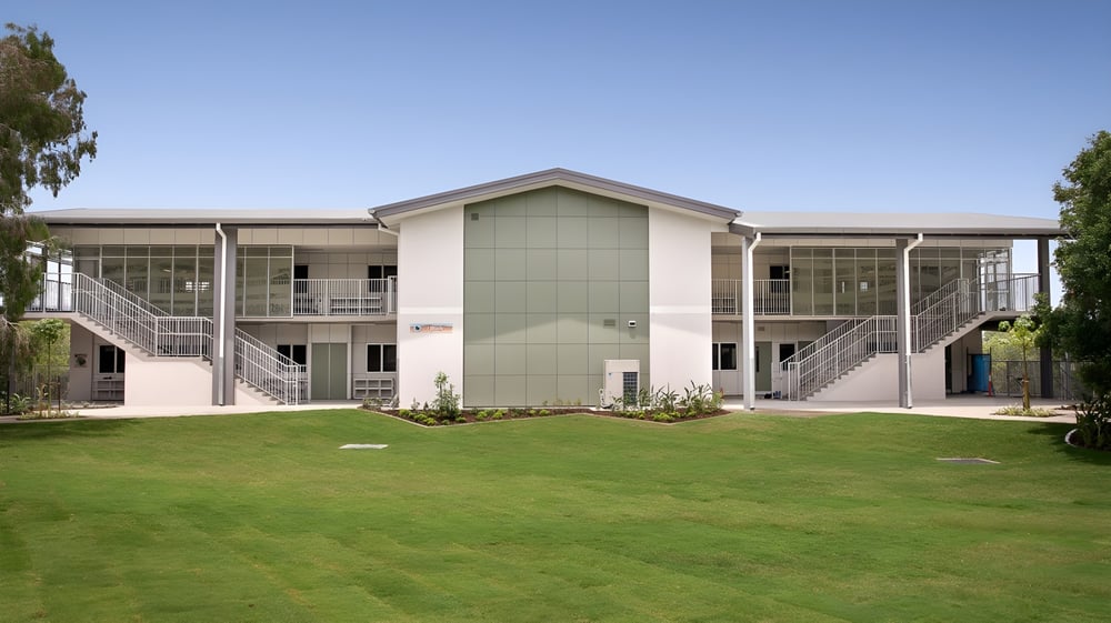 Das moderne zweistöckige Gebäude der Sunshine Beach State High School steht auf einem gepflegten Rasen und ist von grüner Vegetation umgeben.