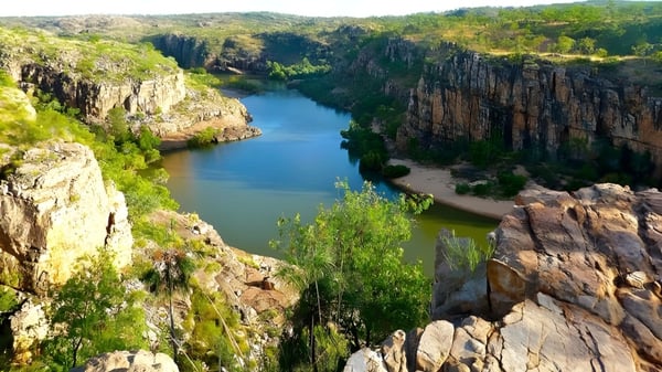 Eine felsige Landschaft mit steilen Klippen und einem türkisfarbenen Fluss führt durch ein grünes Tal auf dem Gelände der Sunshine Beach State High School.