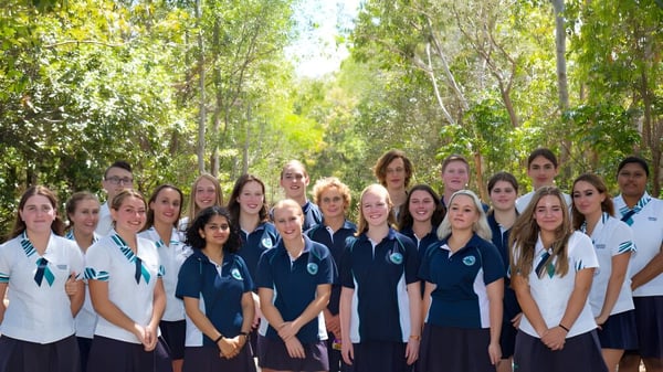 Eine Gruppe Schülerinnen in Schuluniformen steht gemeinsam in einem grünen Wald auf dem Campus der Sunshine Beach State High School.