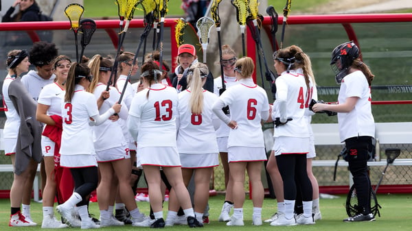 Eine Gruppe von jungen Athletinnen steht auf dem Sportfeld der SUNY Plattsburgh in weißen Trikots mit Nummern.