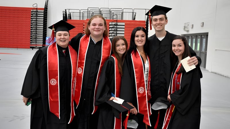 Eine Gruppe von Absolventinnen und Absolventen der SUNY Plattsburgh steht gemeinsam in roten und schwarzen akademischen Gewändern und feiert ihren Abschluss.