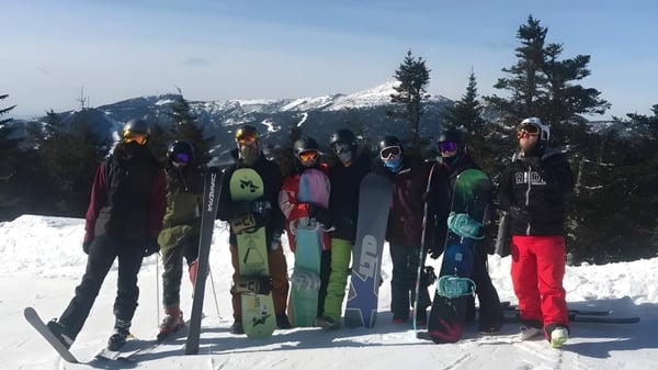 Schüler der SUNY Plattsburgh stehen in bunter Skikleidung vor einer verschneiten Berglandschaft.