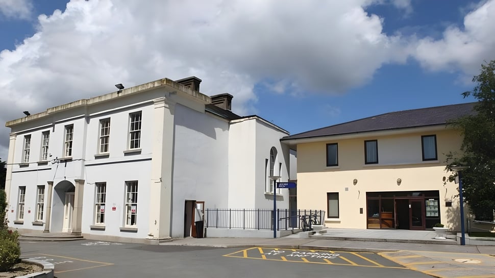 Das zweistöckige weiße Gebäude mit besonderem Architekturstil der Sutton Park School steht vor einem blauen Himmel mit Wolken.
