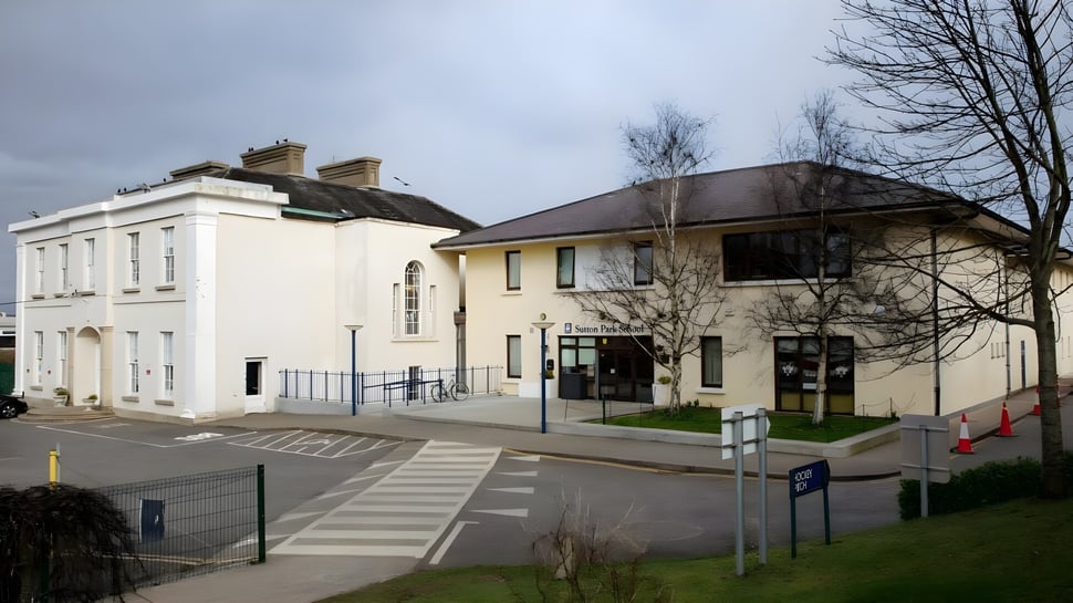 Das mehrstöckige weiße Gebäude mit geneigtem Dach der Sutton Park School in Dublin ist von kahlen Bäumen umgeben.