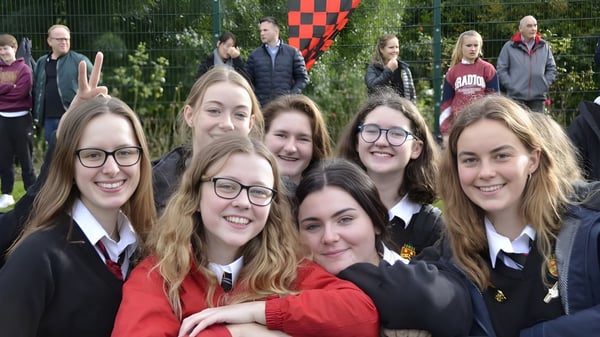 Eine Gruppe Schülerinnen der Sutton Park School steht gemeinsam in einem parkähnlichen Bereich mit Bäumen und einer rot-weiß karierten Fahne im Hintergrund.