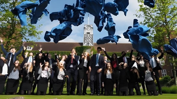 Absolventen der Sutton Valence School in schwarzen Talaren stehen vor einer großen abstrakten Skulptur im Freien.