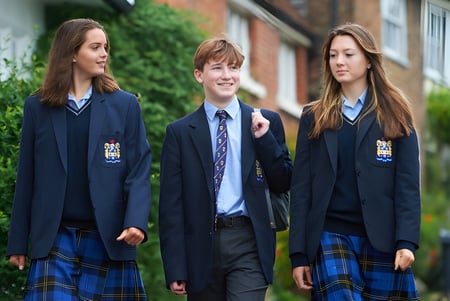 Drei Schülerinnen und Schüler der Sutton Valence School gehen gemeinsam auf einem Weg neben einem Backsteingebäude.