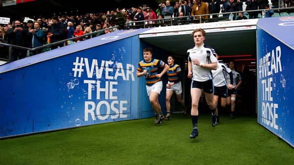 Schüler der Sutton Valence School gehen über ein Feld vor einem großen #WearTheRose-Banner mit Zuschauern im Hintergrund.