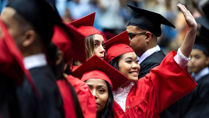 Eine Gruppe von Absolventinnen und Absolventen der Sydenham High School feiert in roten Talaren und Hüten mit erhobenen Händen.