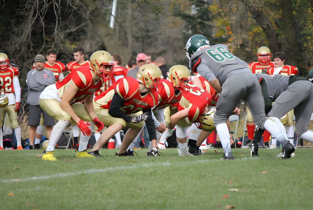 Schüler der Sydenham High School spielen ein Footballspiel auf dem Spielfeld vor herbstlicher Waldkulisse.