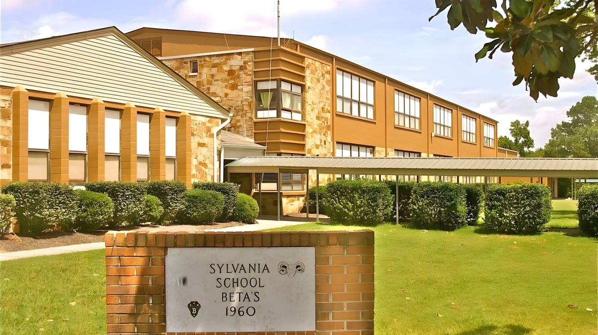 Das zwei Stockwerke hohe Gebäude der Sylvania High School mit Backstein- und Seitenverkleidung ist von gepflegtem Gras und Sträuchern umgeben.