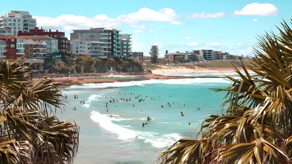 Menschen genießen das klare blaue Wasser am Strand von Sylvania High School mit Hochhäusern und Palmen im Hintergrund.