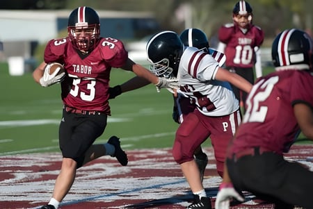 Schüler der Tabor Academy spielen ein Footballspiel auf dem Spielfeld mit roter und weißer Sportkleidung.