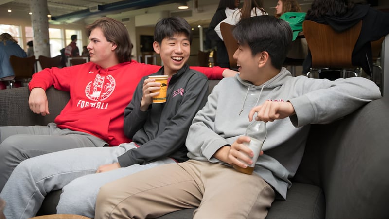 Drei Schülerinnen und Schüler sitzen gemeinsam in einem öffentlichen Bereich auf dem Campus der Tabor Academy und unterhalten sich.