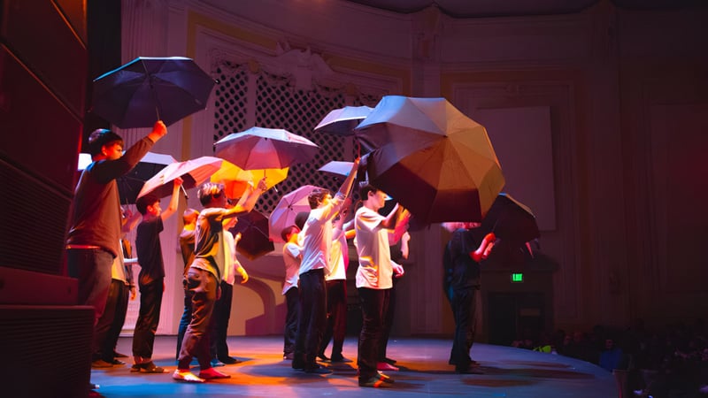 Eine Gruppe von Schülerinnen und Schülern der Tacoma Public Schools hält bunte Regenschirme auf einer Bühne mit dramatischer Beleuchtung.