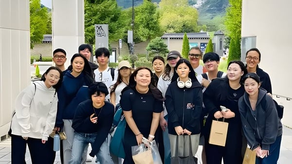 Eine Gruppe junger Menschen steht vor einem Gebäude mit Bäumen auf dem Campus der Taejon Christian International School.